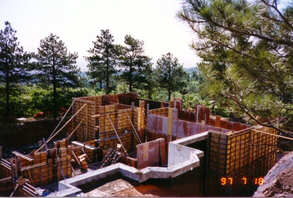 A construction site with wooden concrete forms set up for a building foundation amidst a forest of pine trees.
