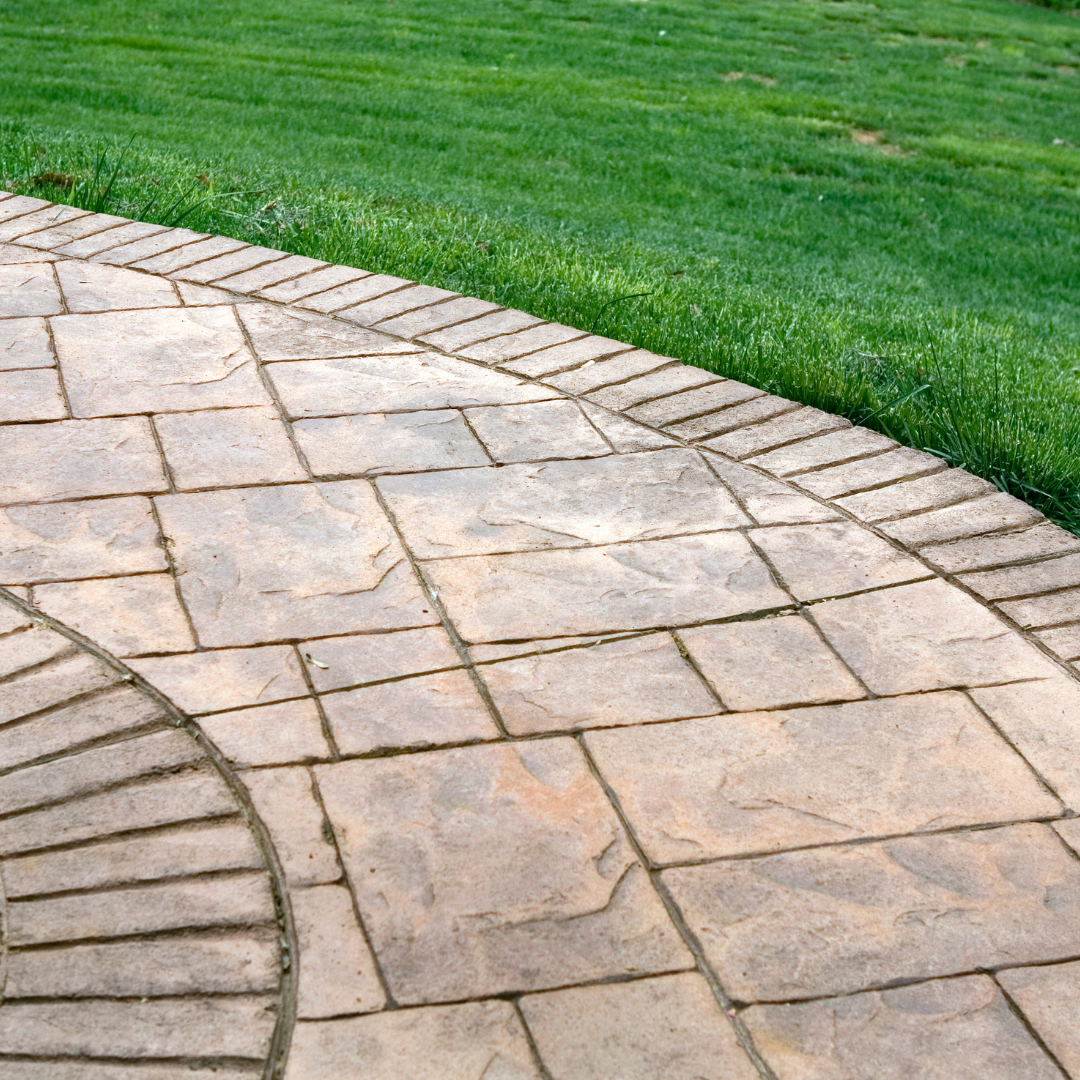 A patterned concrete patio with a decorative border stone edge, meeting a lush green grass lawn.
