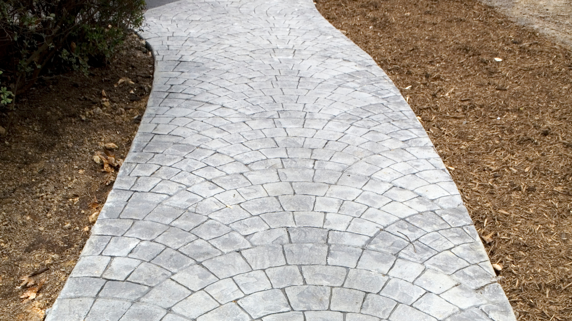 A gray, stone-paved walkway with a fan-shaped pattern, flanked by brown mulch on both sides.