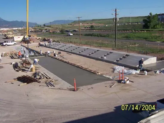 Construction workers pour concrete for a long, stepped structure at an outdoor industrial site on July 14, 2004.