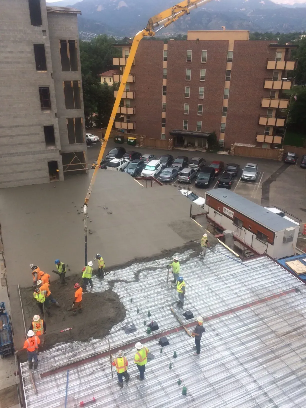 A crew in hard hats and high-visibility vests uses a concrete pump to pour a new floor on a construction site.