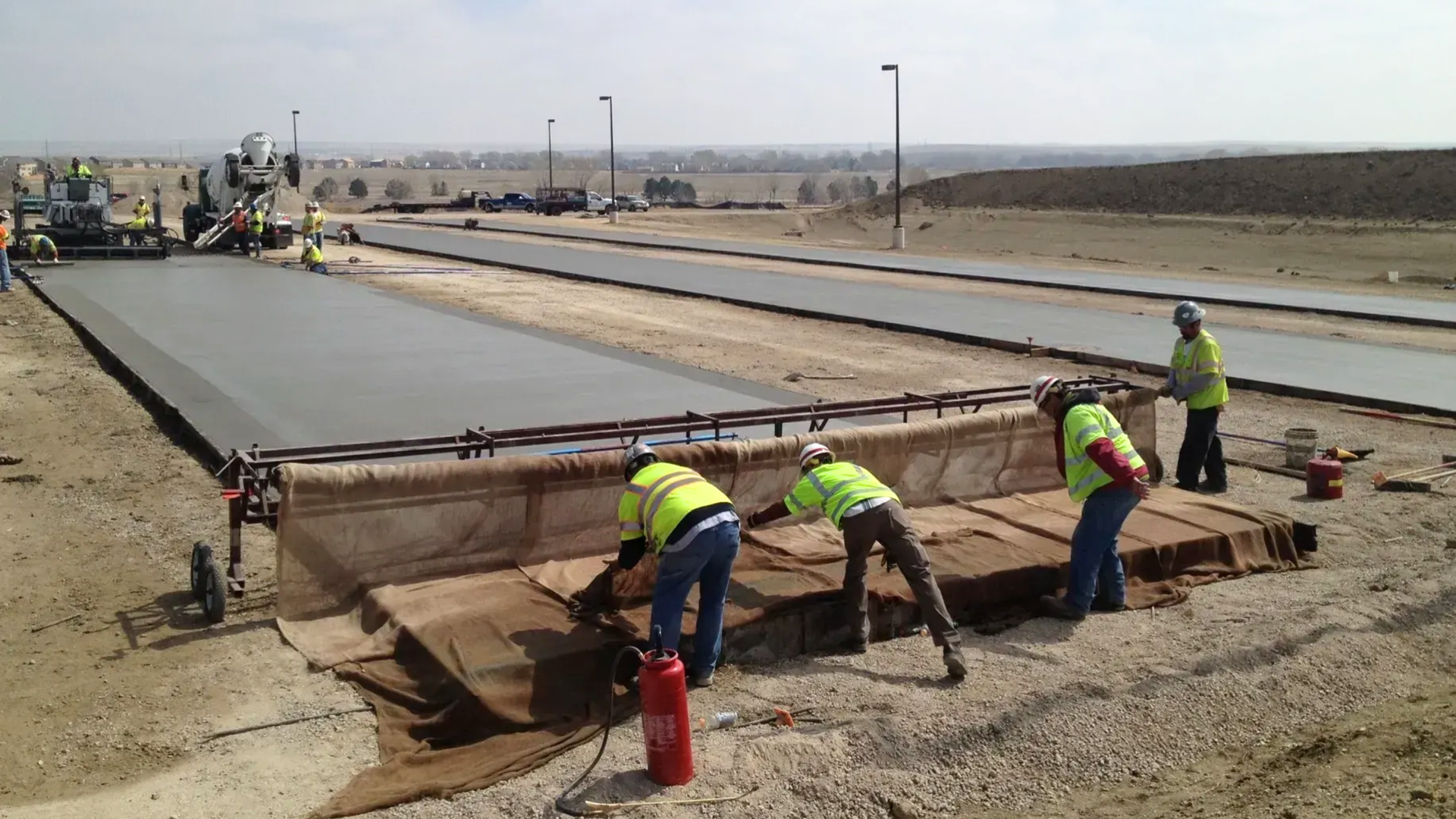 Construction workers using a burlap drag to texture a freshly poured concrete road.