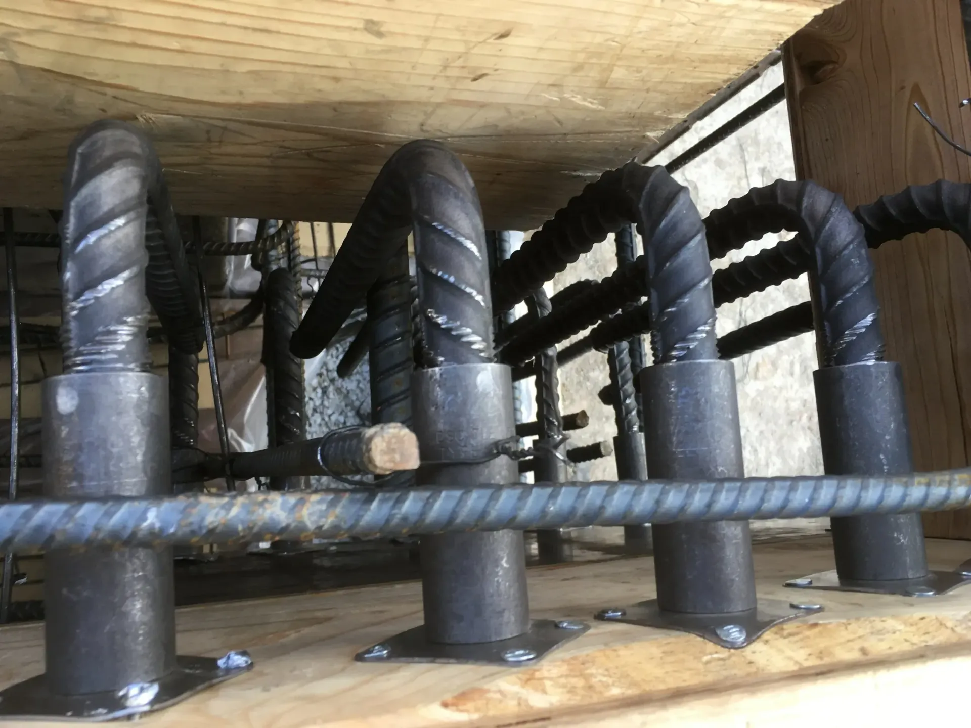 Rebar dowels secured to a wooden formwork by metal sleeves, preparing for a concrete pour.