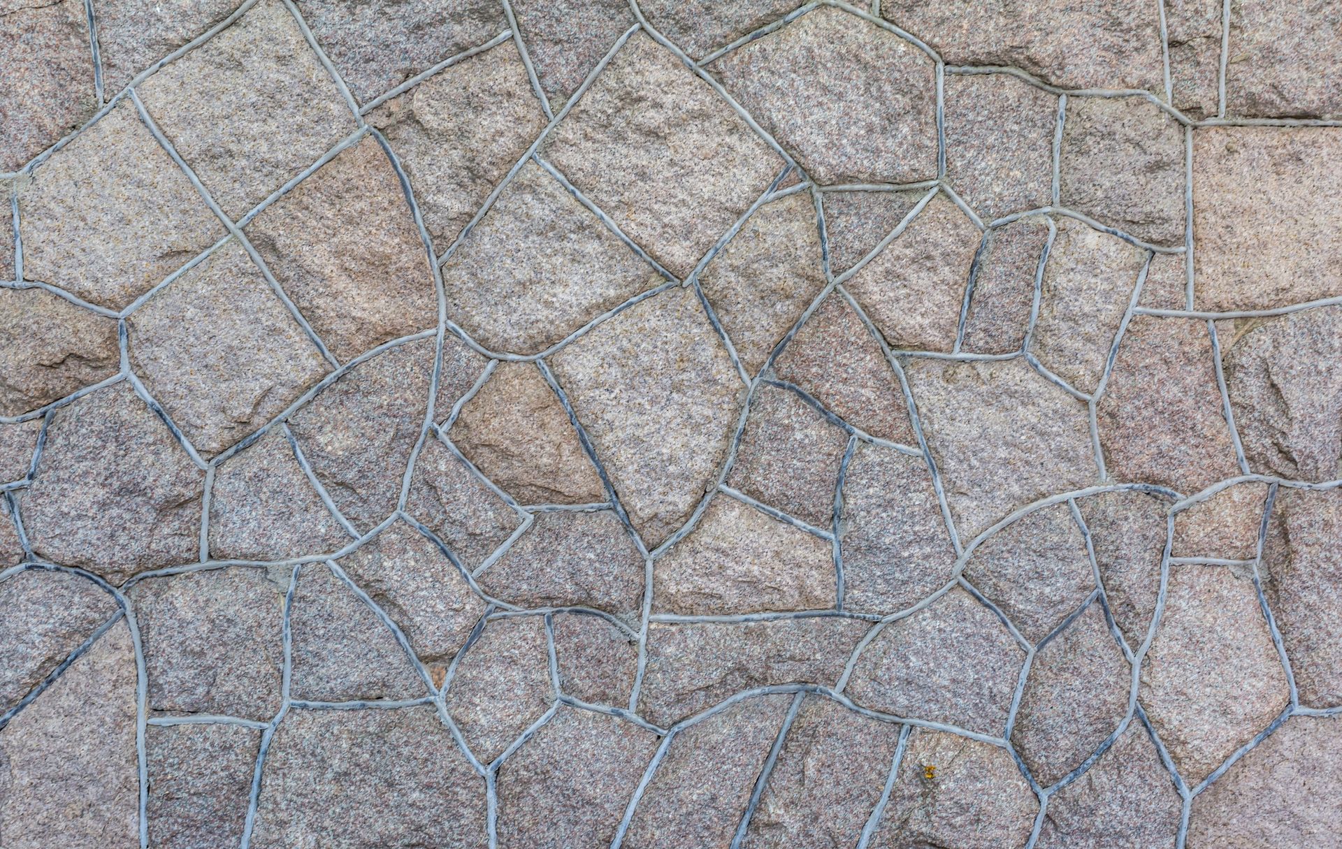 A close-up view of a textured stone wall featuring irregularly shaped, grey-brown rocks fitted together with dark mortar.