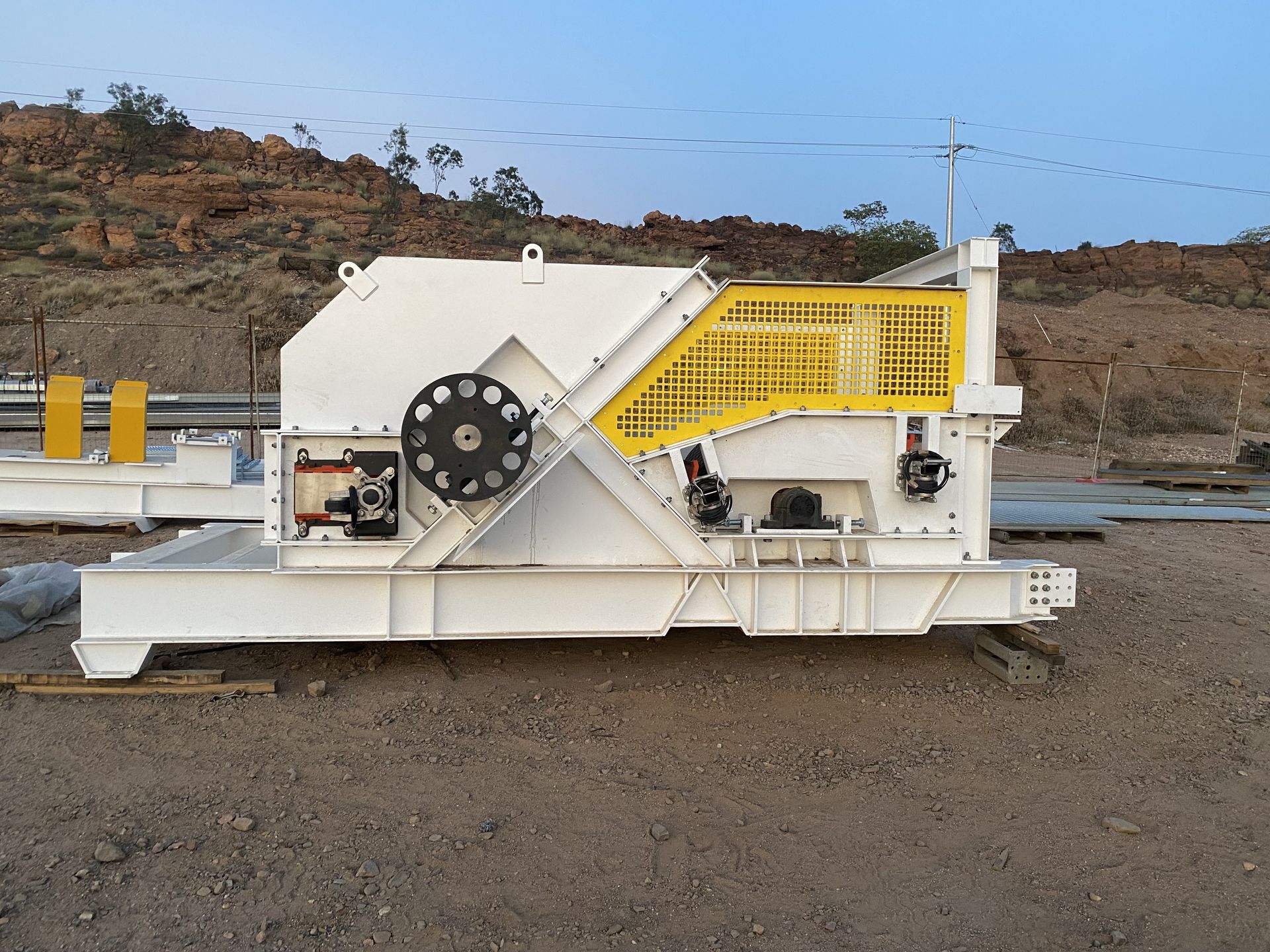 White industrial rock crusher with yellow safety rails on a gravel lot outdoors