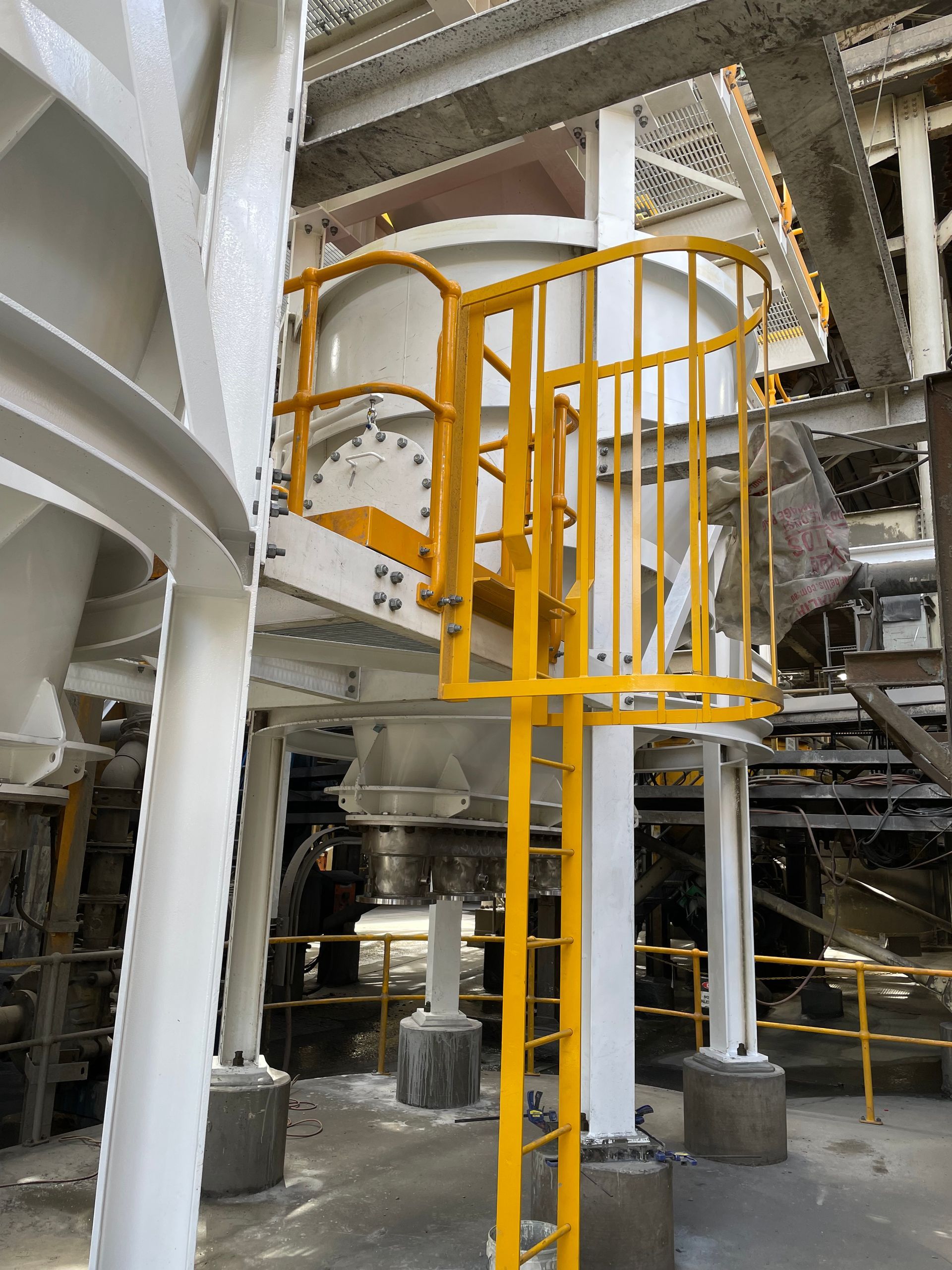 Yellow industrial platform and stairs inside a large factory with metal pipes and machinery.