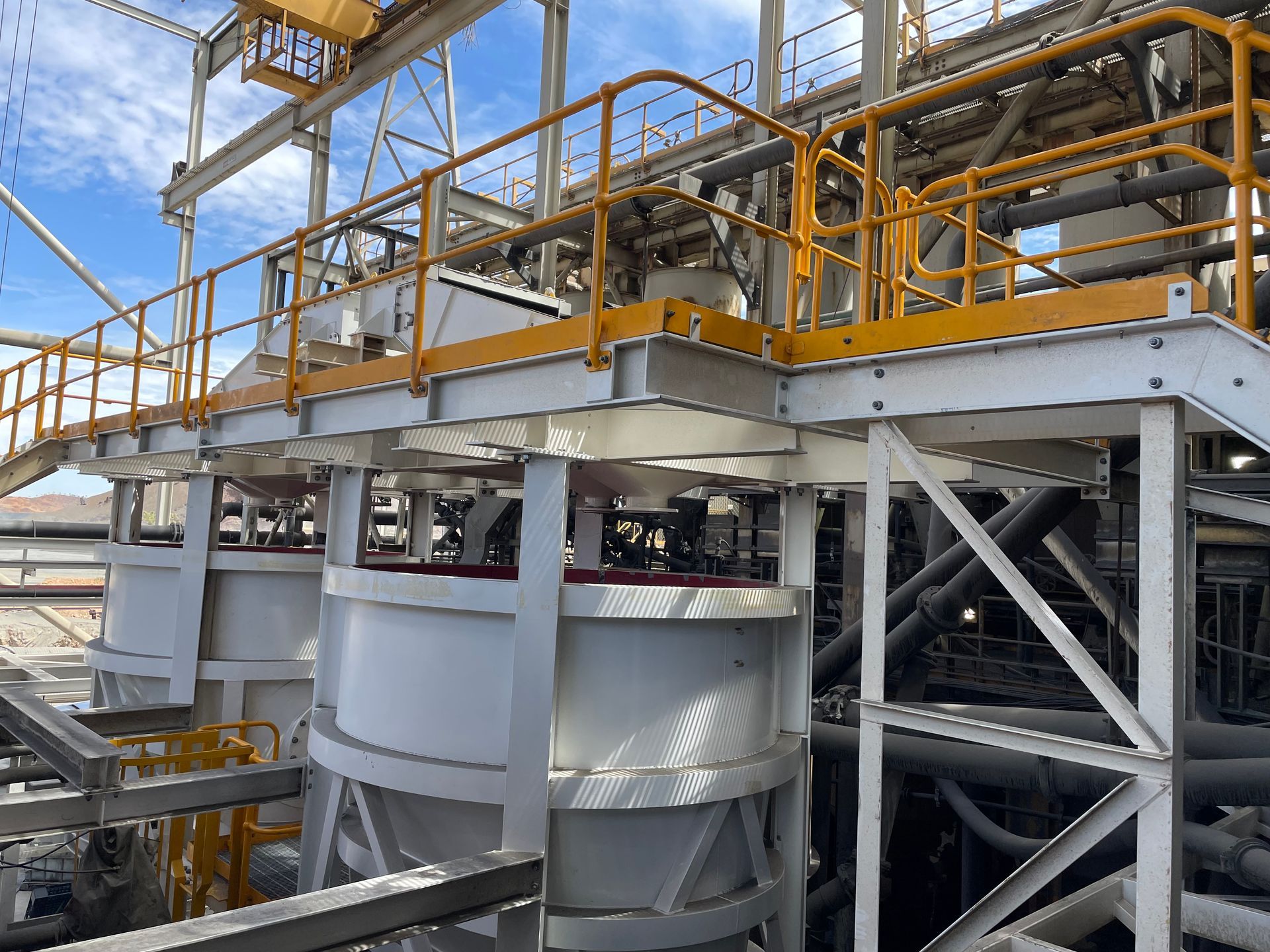 Industrial plant machinery with yellow railings and large steel tanks under a blue sky