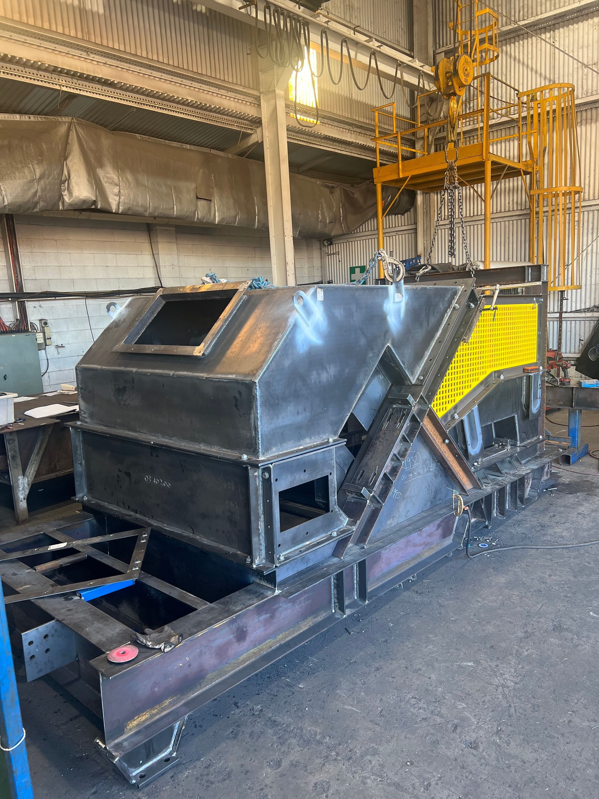 Industrial machine with black metal housing and yellow framework inside a factory warehouse