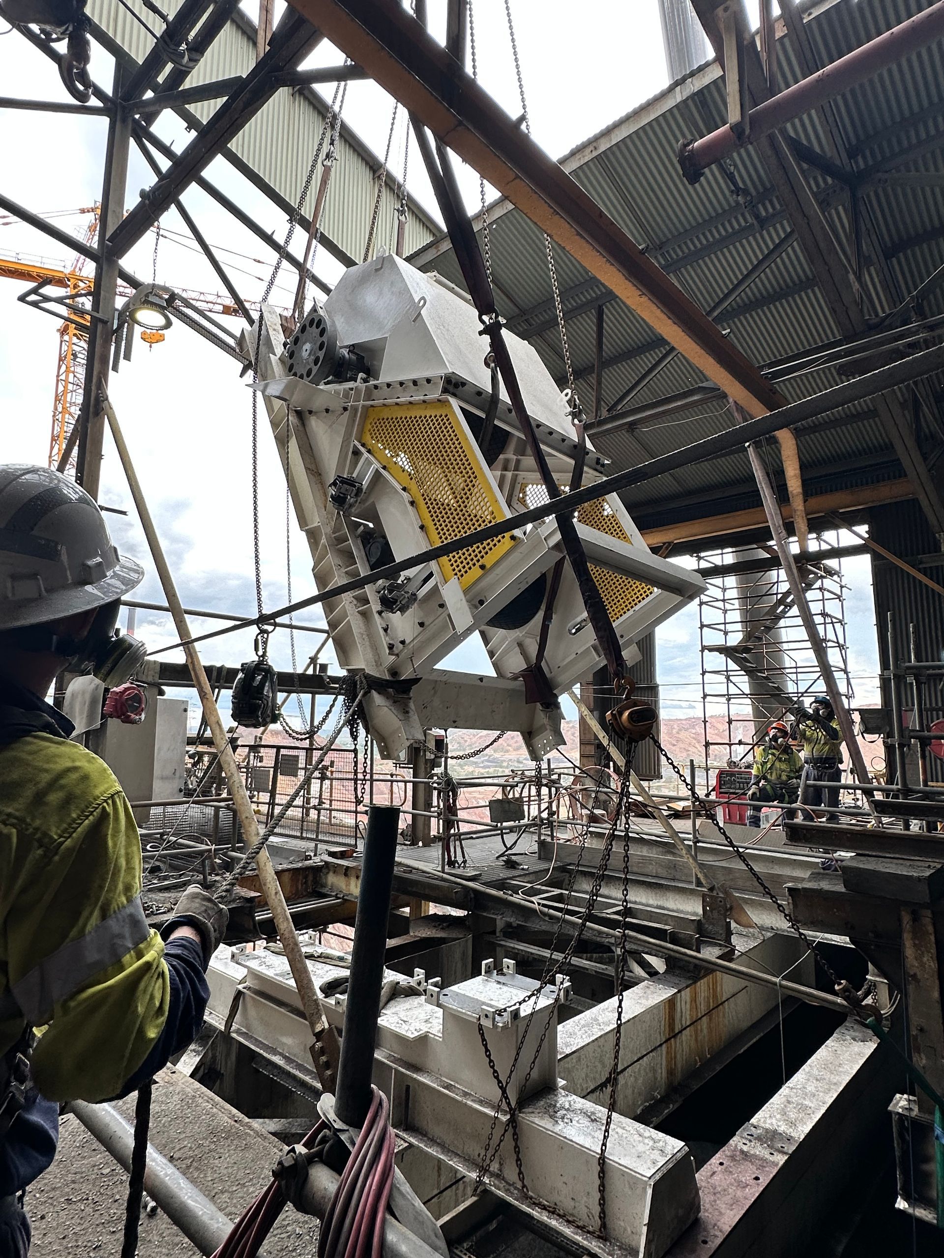 Worker in hard hat near suspended machinery inside an industrial construction site.