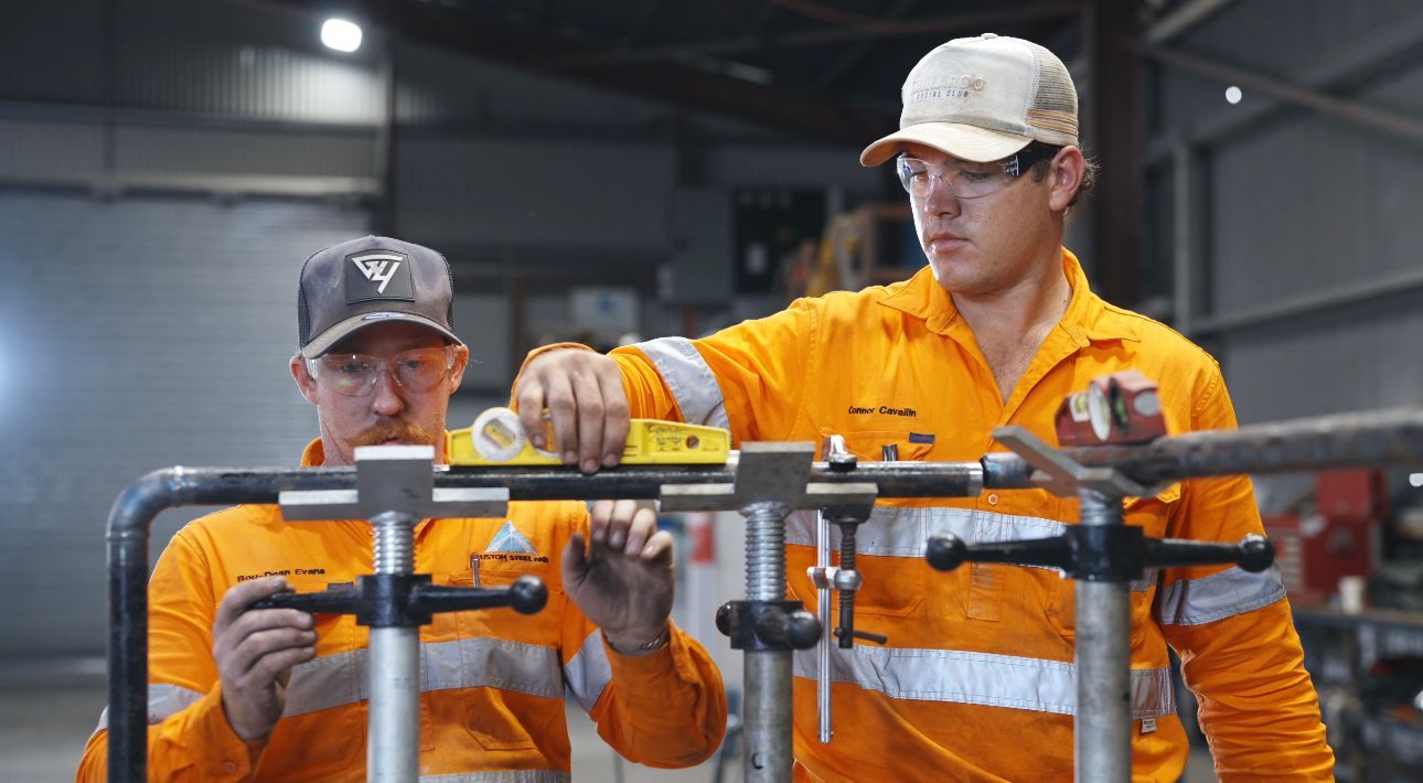Two workers in orange safety gear inspect machinery in an industrial workshop