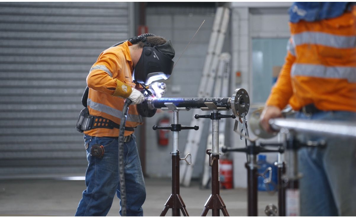 Worker in Orange Jacket Using a Power Tool on a Metal Pipe in a Workshop — Custom Steel Fab in Bohle, QLD