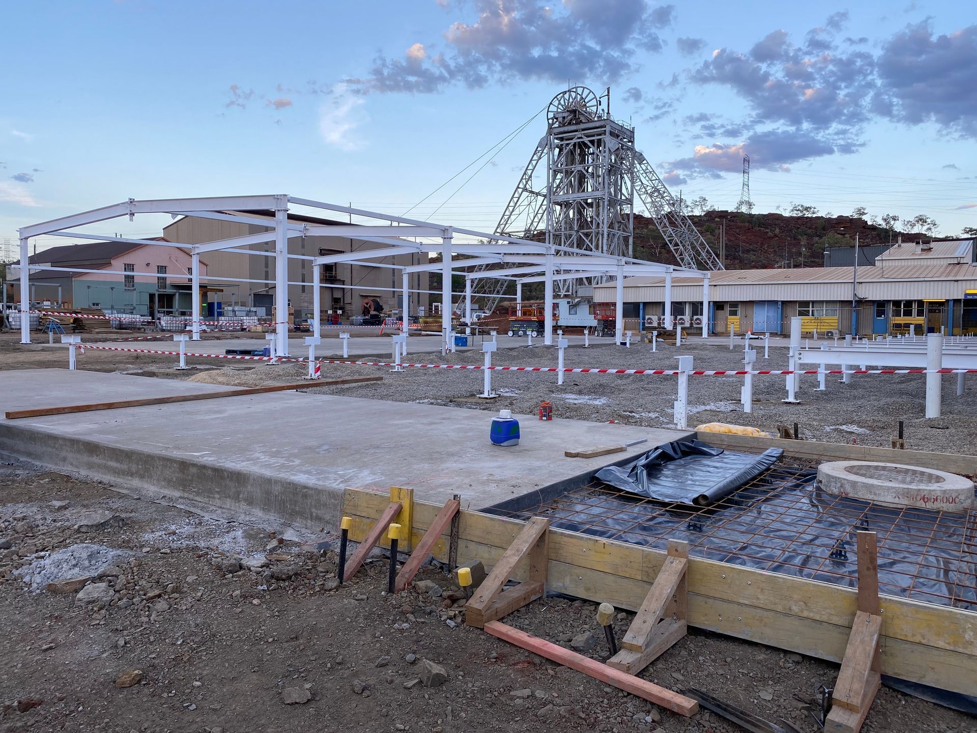 Construction site with steel framework, concrete forms, and a crane under a cloudy sky.