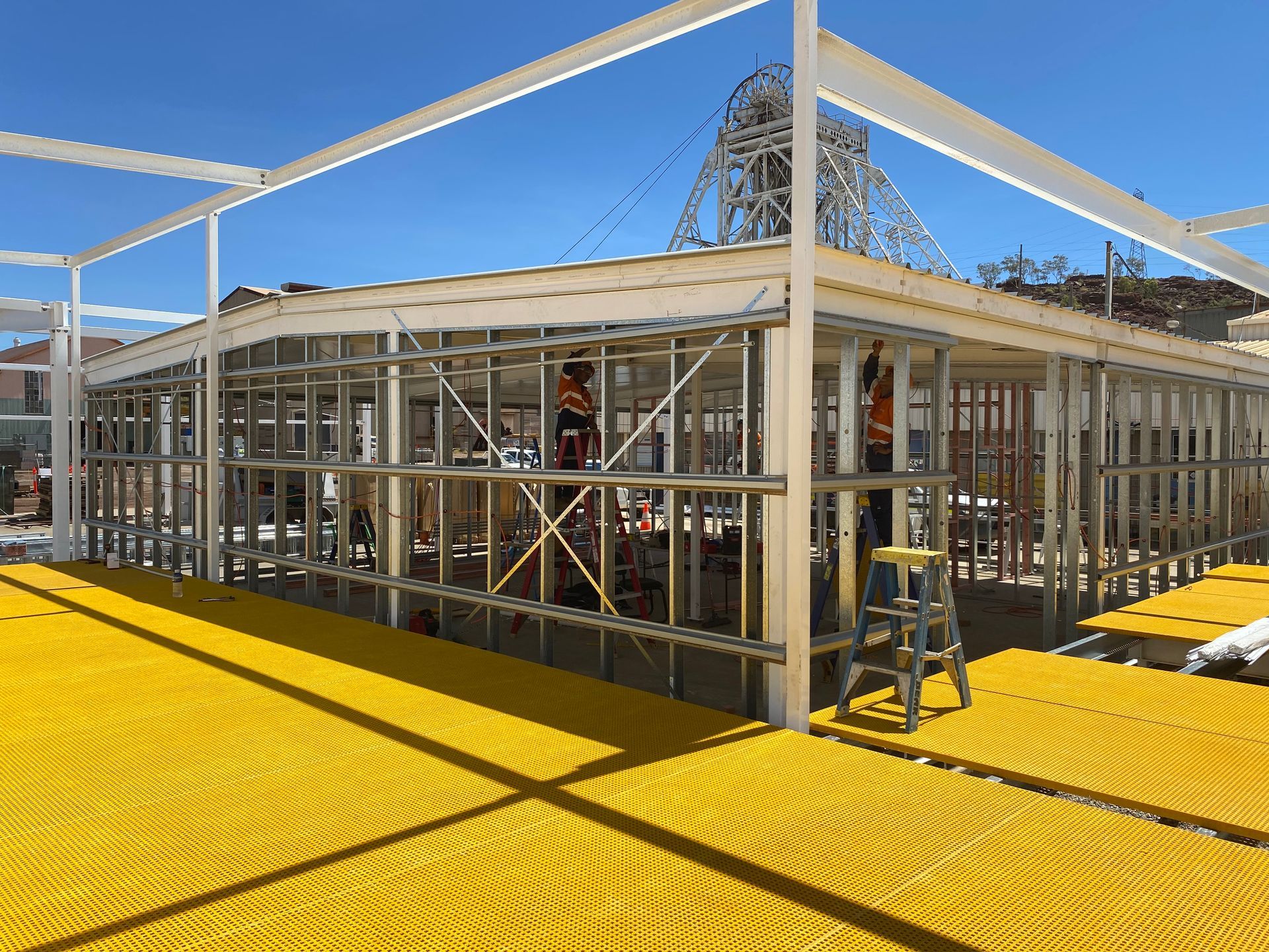 Steel-framed building under construction with workers and bright yellow safety flooring
