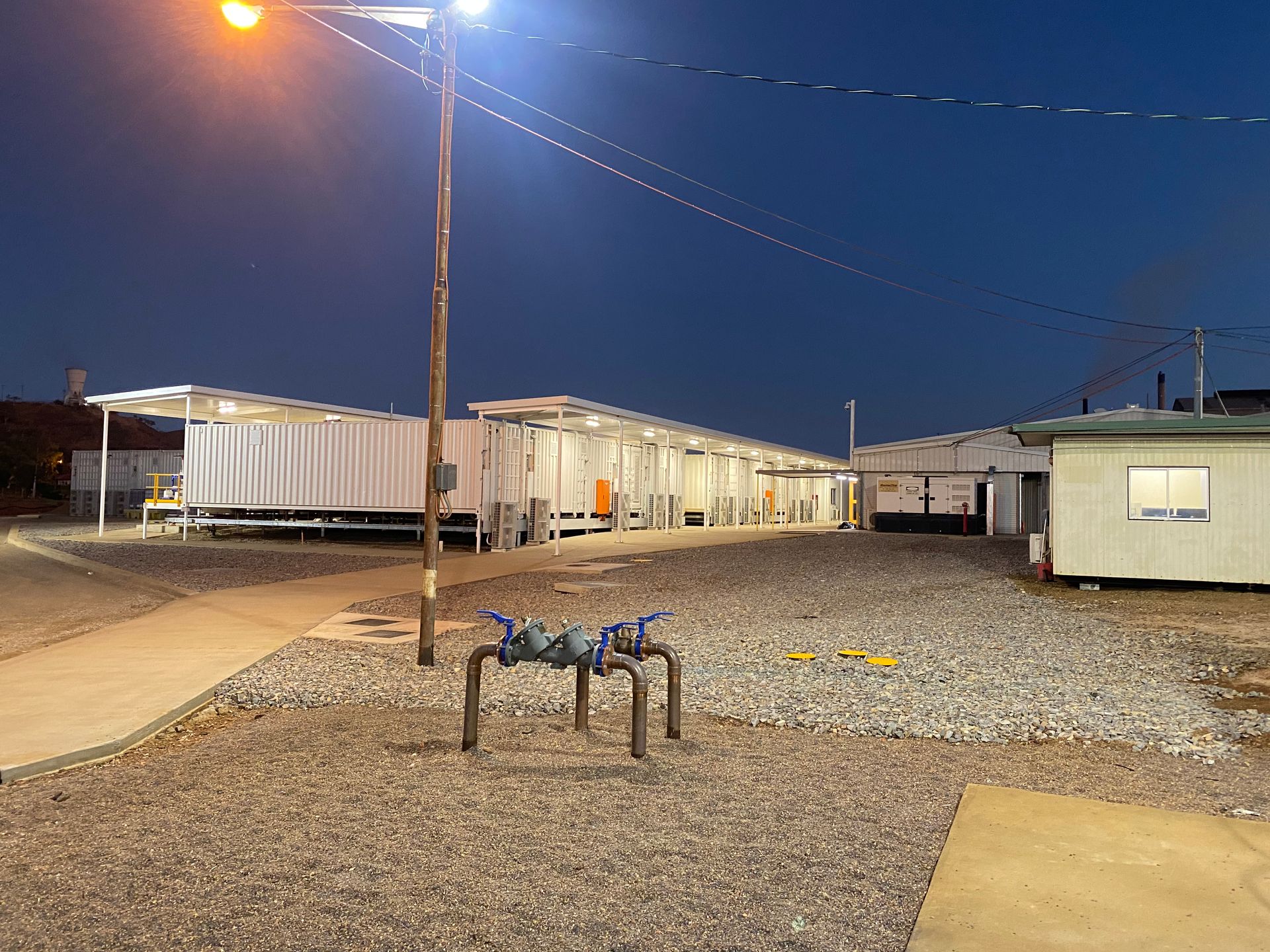 Gravel lot at dusk with white trailers, a lamppost, and a small table in the foreground