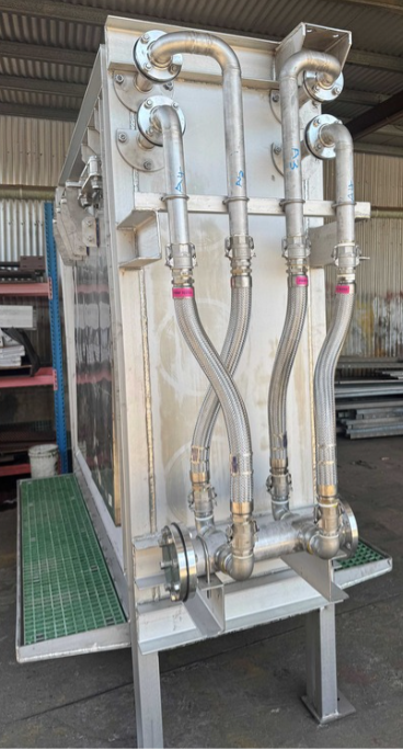 Industrial stainless-steel filtration unit with pipes and hoses on a metal platform in a workshop