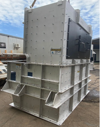 Large industrial metal equipment unit on a construction site, gray and black with bolted panels and a base frame
