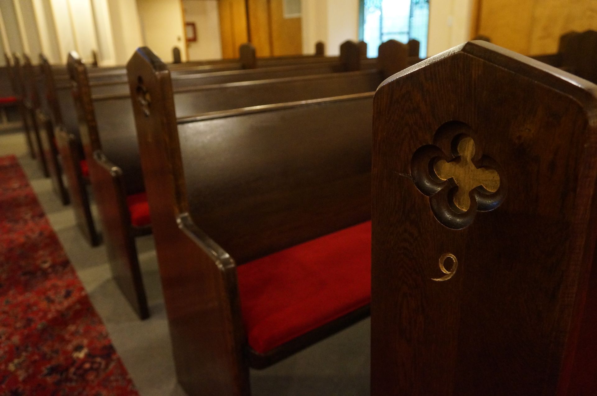 Rows of wooden church pews with red cushions, featuring a carved clover design on the end of a pew marked with the number 9.