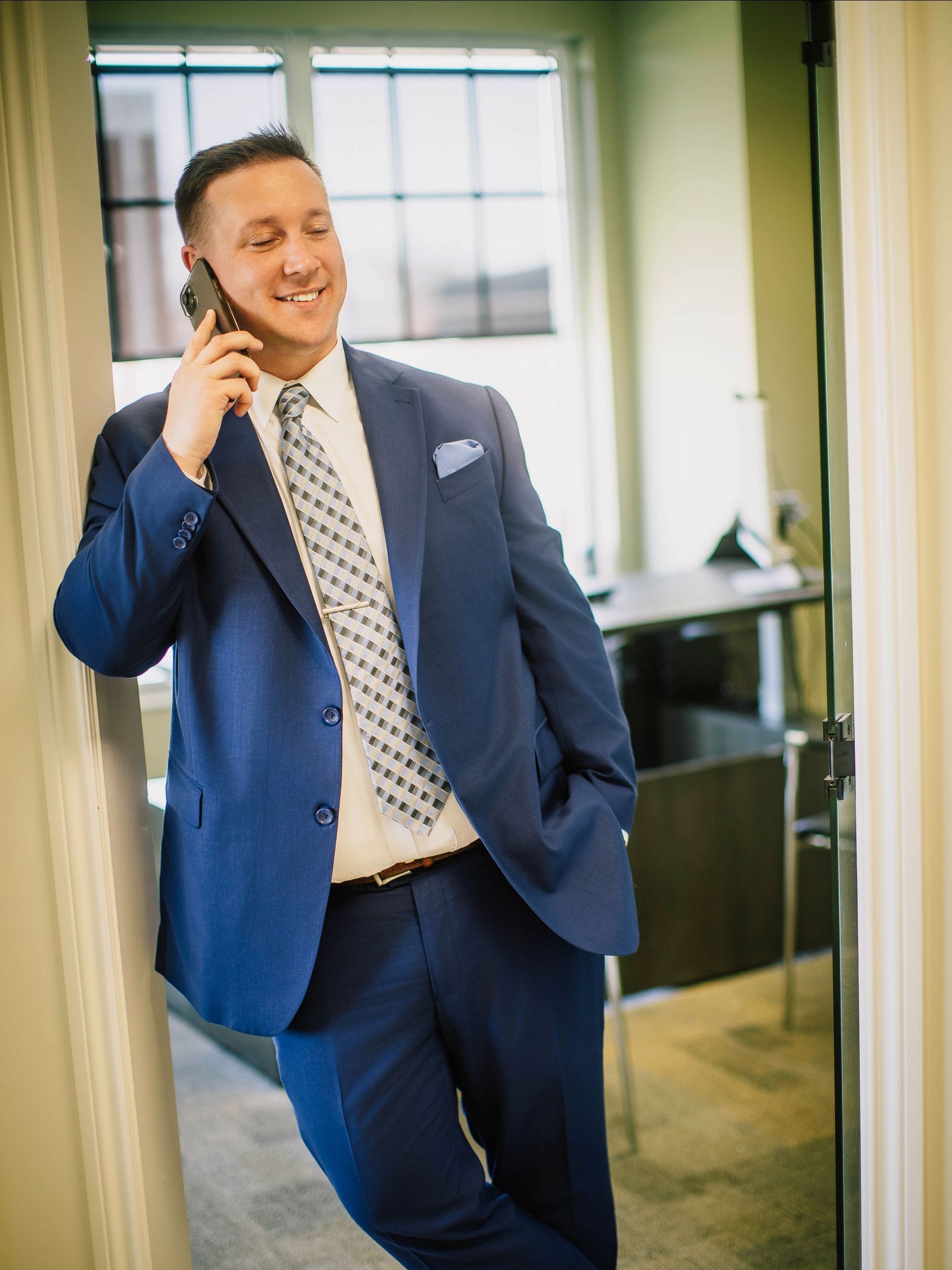 A man in a blue suit and tie is talking on a cell phone.