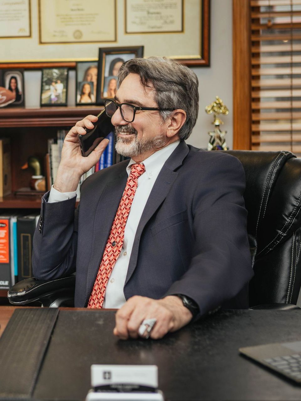A man in a suit and tie is sitting at a desk talking on a cell phone.