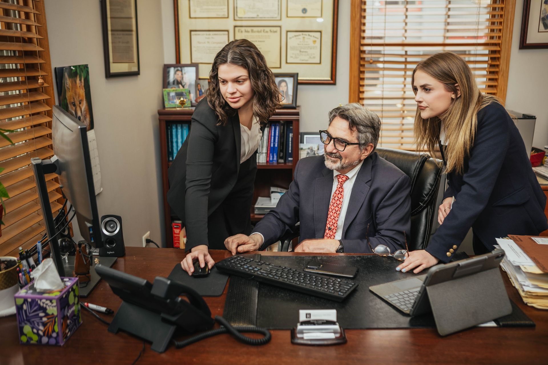 A man and two women are standing around a desk looking at a computer screen.