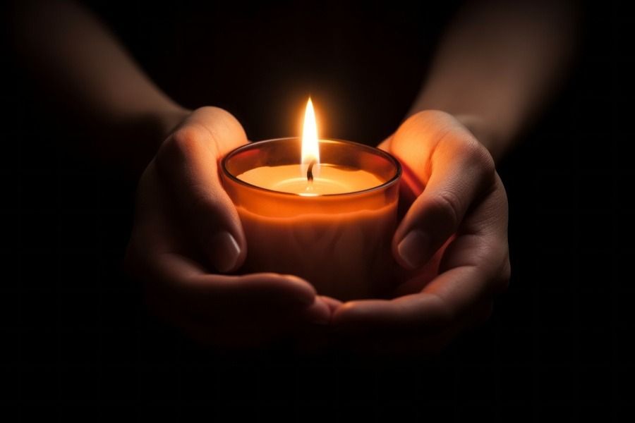 Hands cupping a lit candle in a dark setting