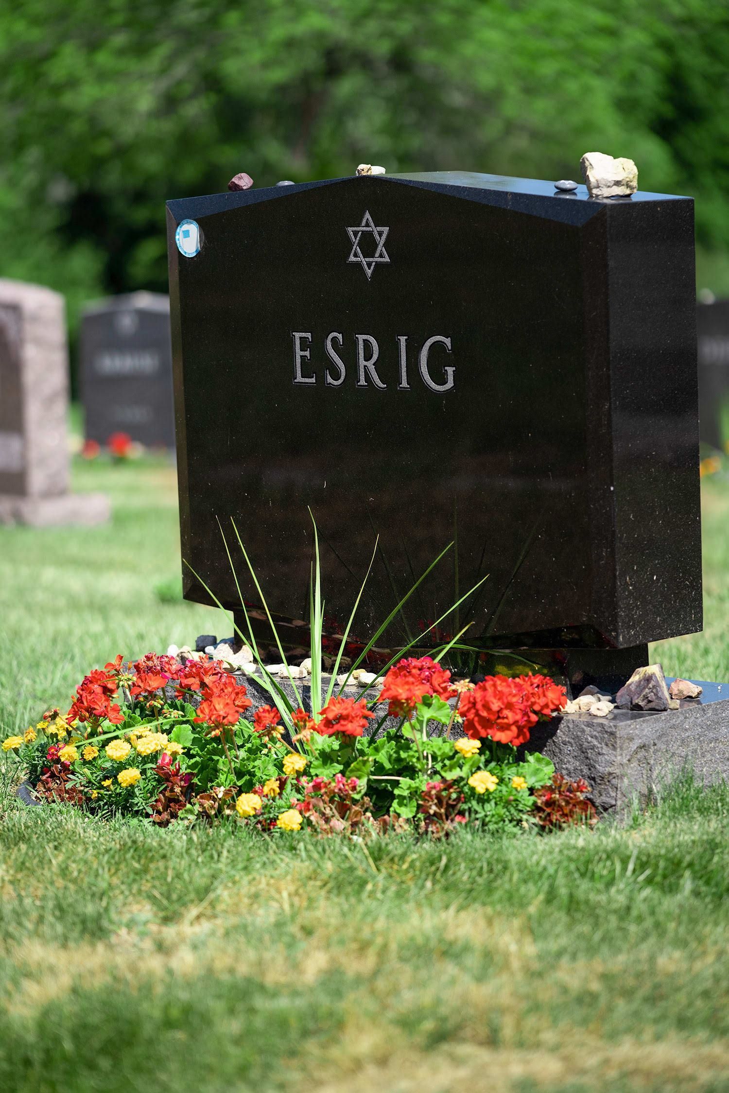 Black gravestone marked “ESRIG” with flowers at the base in a cemetery.