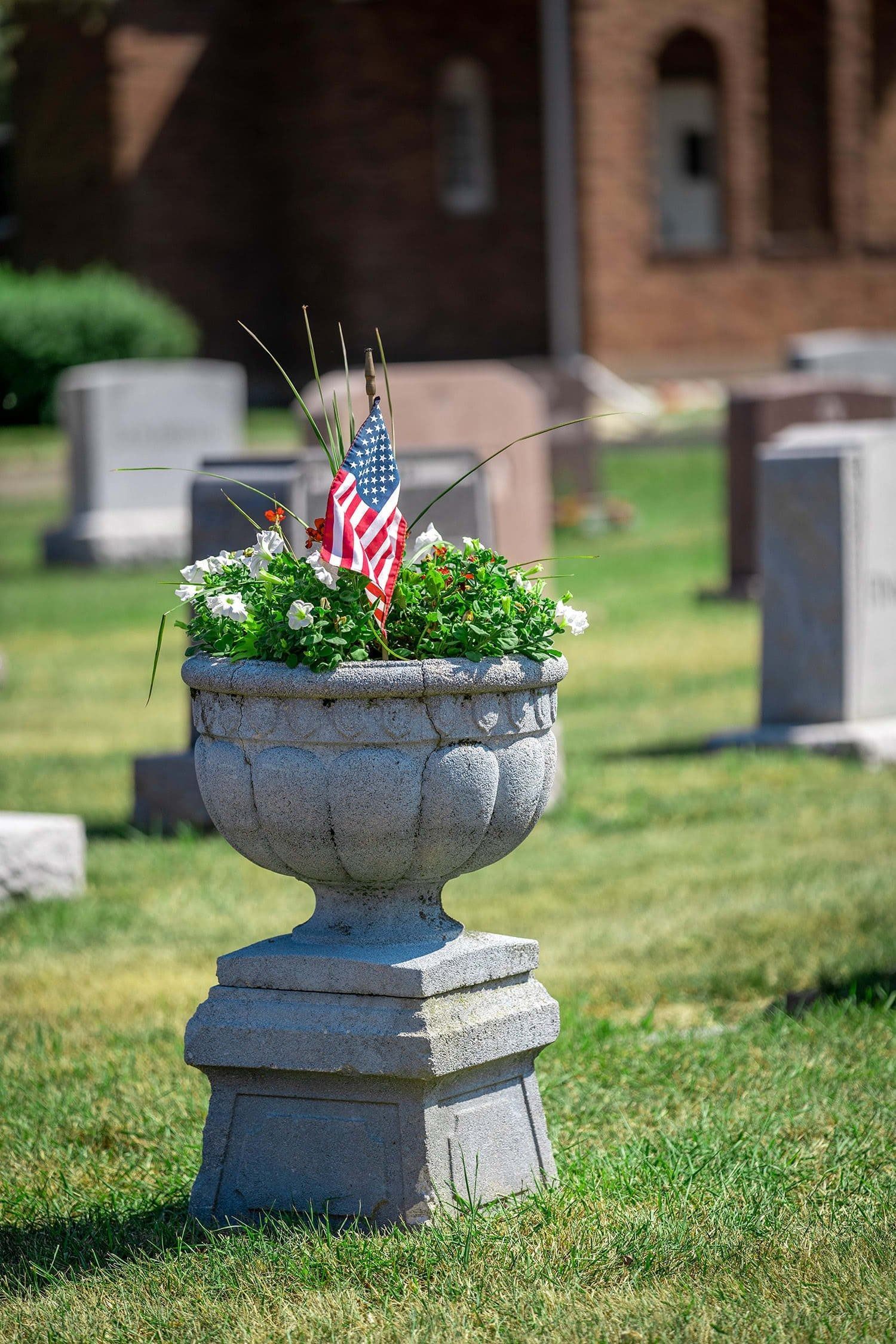 Stone planter with flowers and small American flags in a cemetery lawn