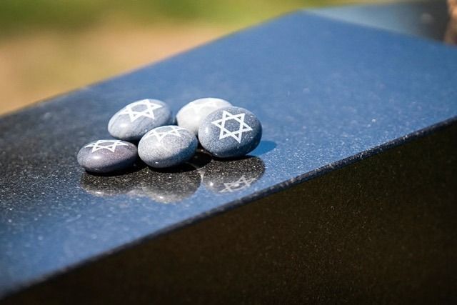 Four small gray stones with white Star of David symbols on a blue surface