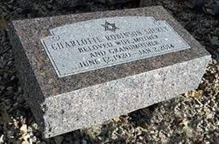 Granite gravestone with engraved plaque on a rocky ground in bright sunlight