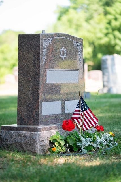 Gravestone with American flag and red flowers in a sunlit cemetery