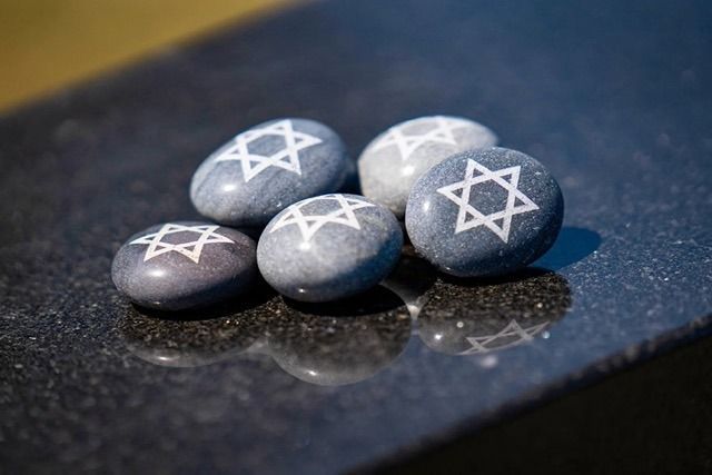 Four gray pebbles with white Star of David symbols on a dark reflective surface.