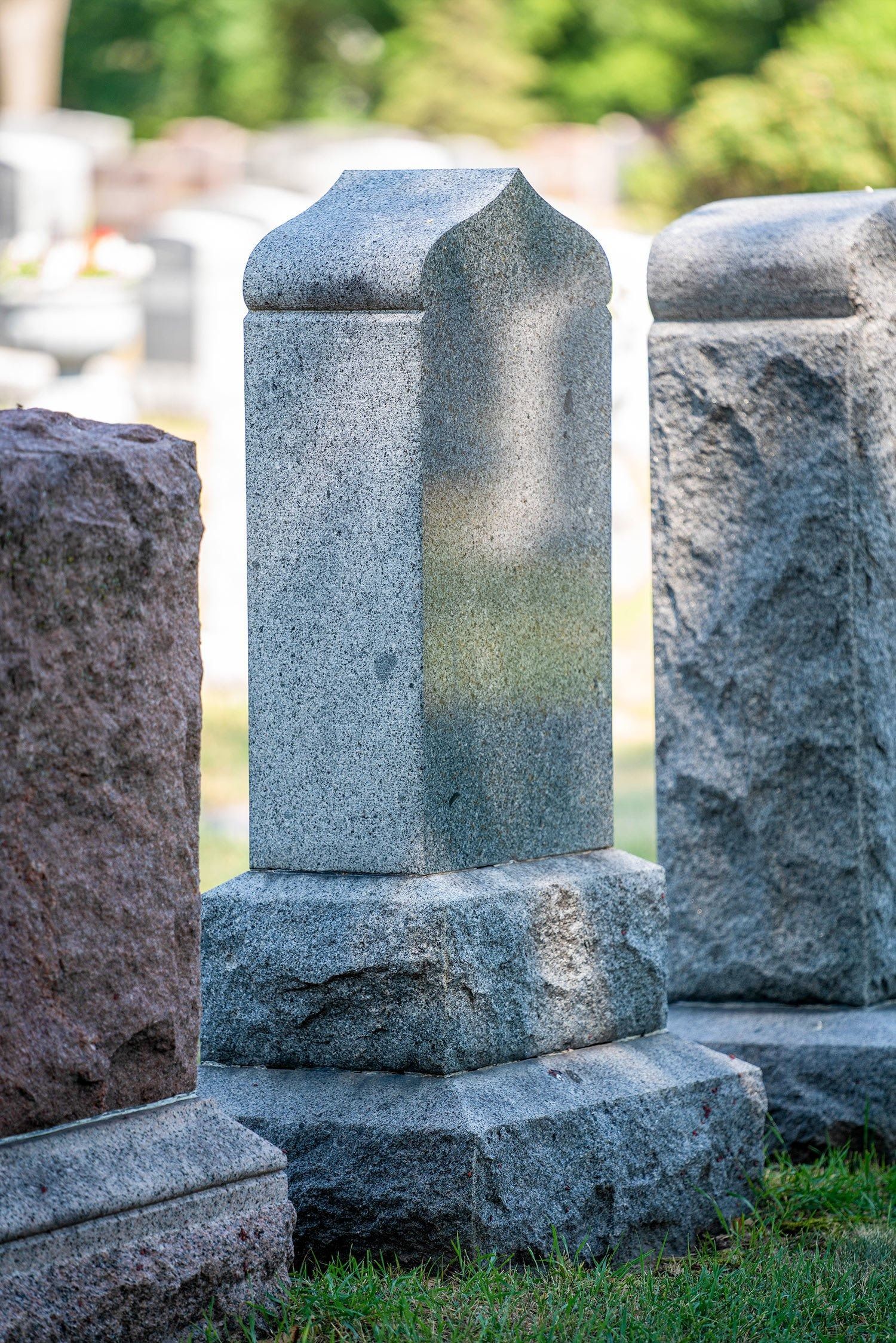 Weathered stone grave markers in a cemetery, with a blue-gray monument centered on grass.