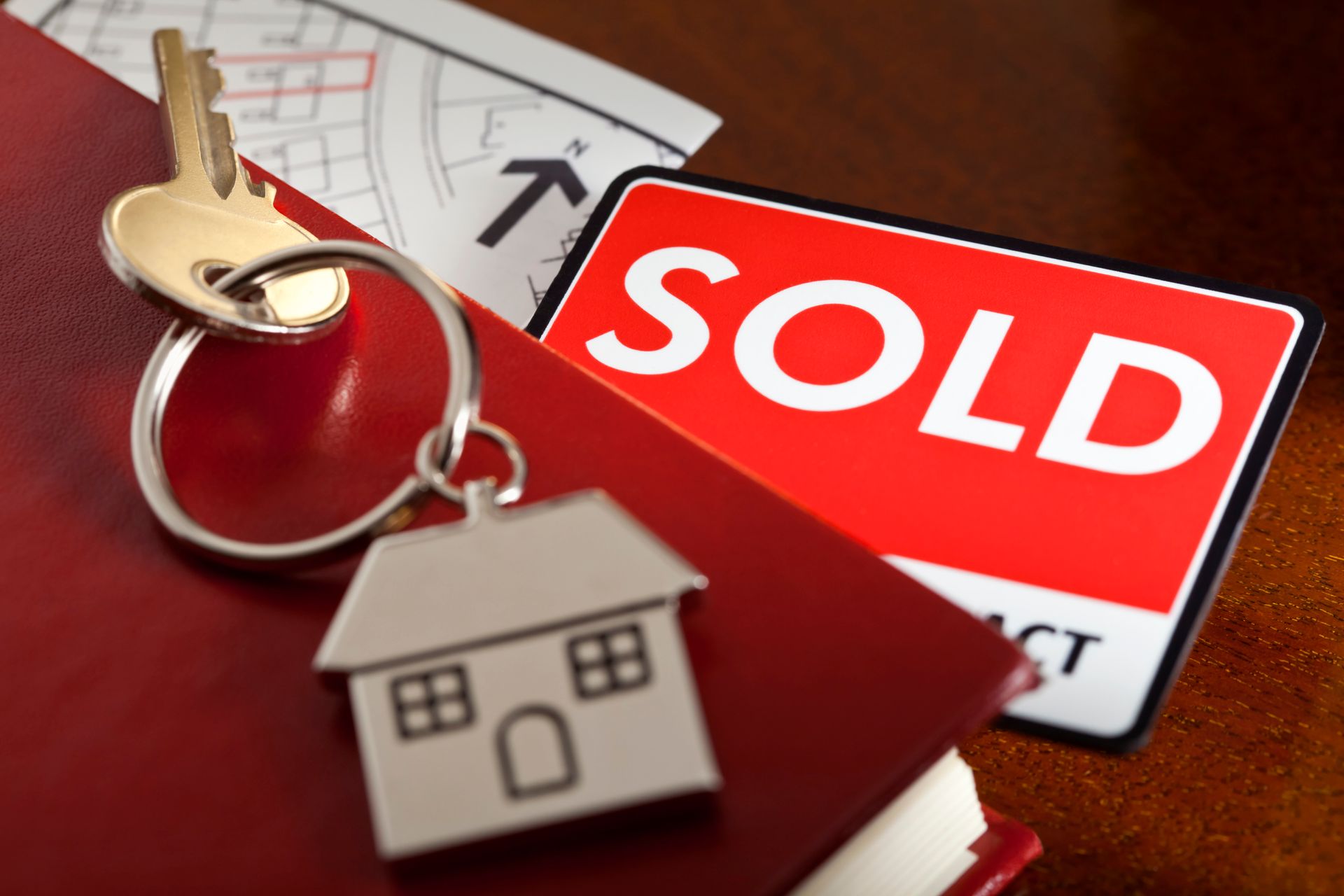 House key on red book with “SOLD” sign in background.