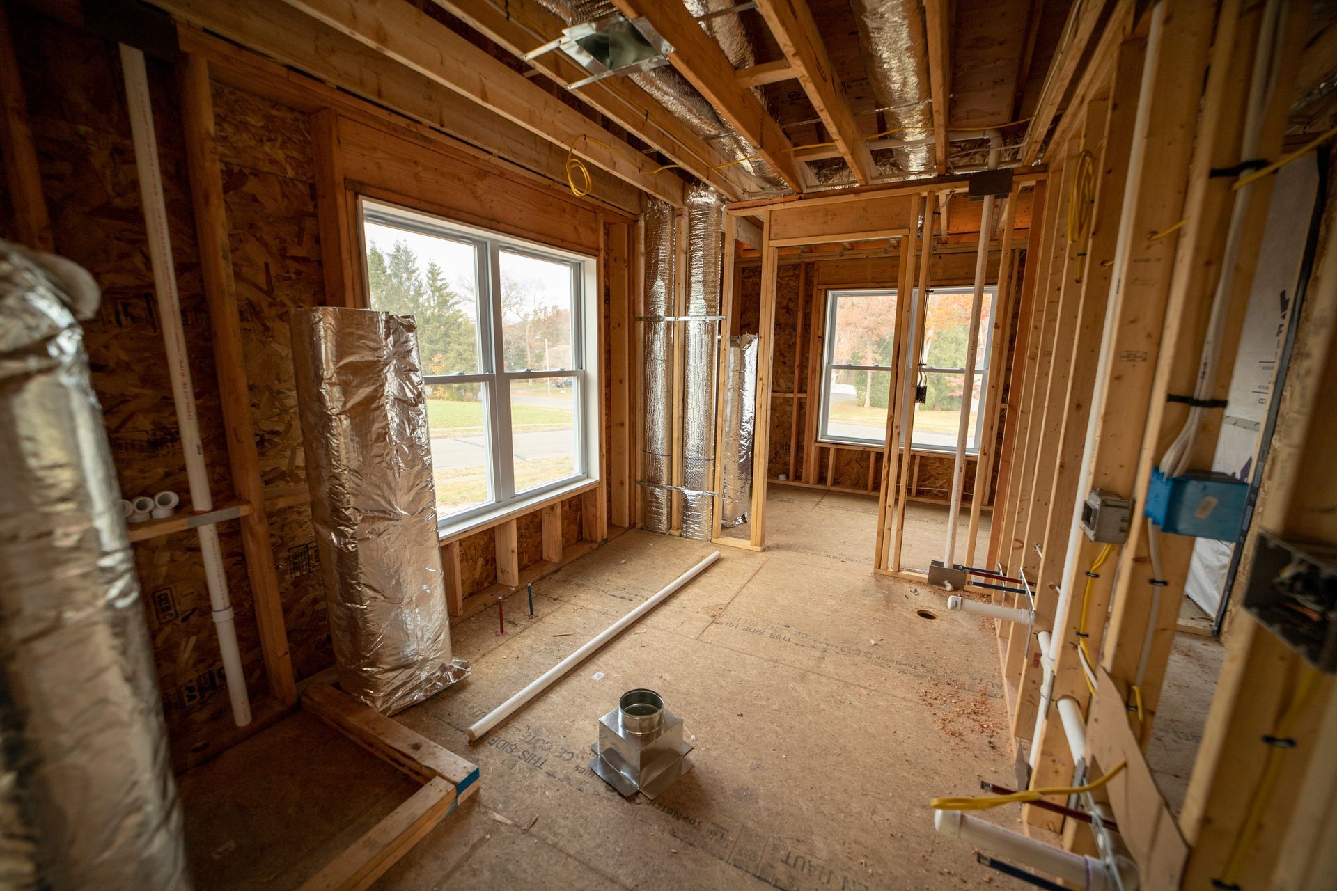 Unfinished room under renovation with exposed studs, insulation, and large windows letting in daylight