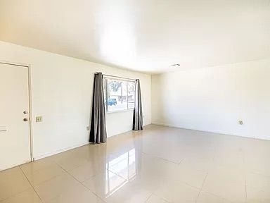 Empty bright living room with white walls, glossy tile floor, and a window with gray curtains.