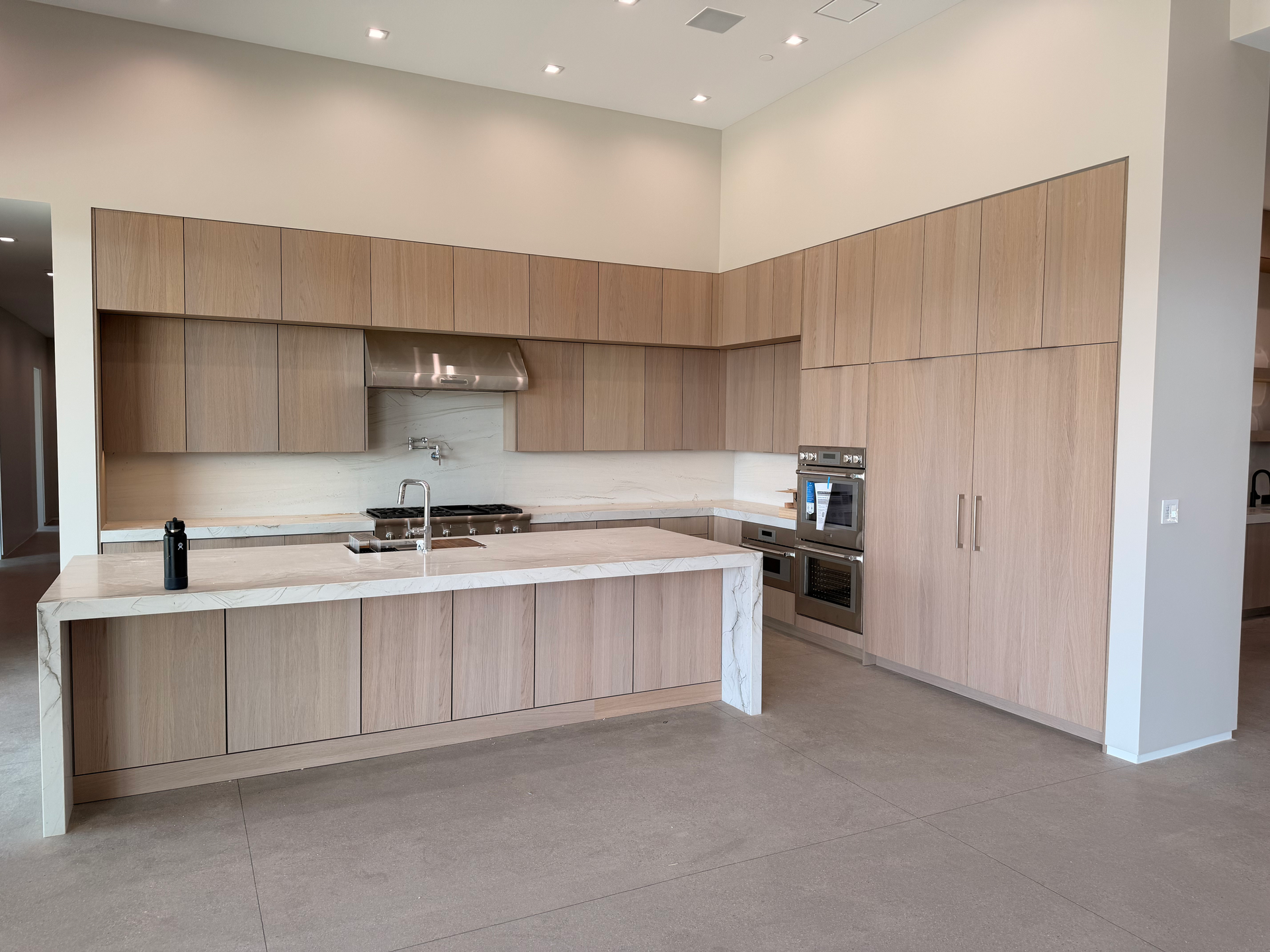 Modern kitchen with light wood cabinets, white island, built-in oven, and gray carpeted floor