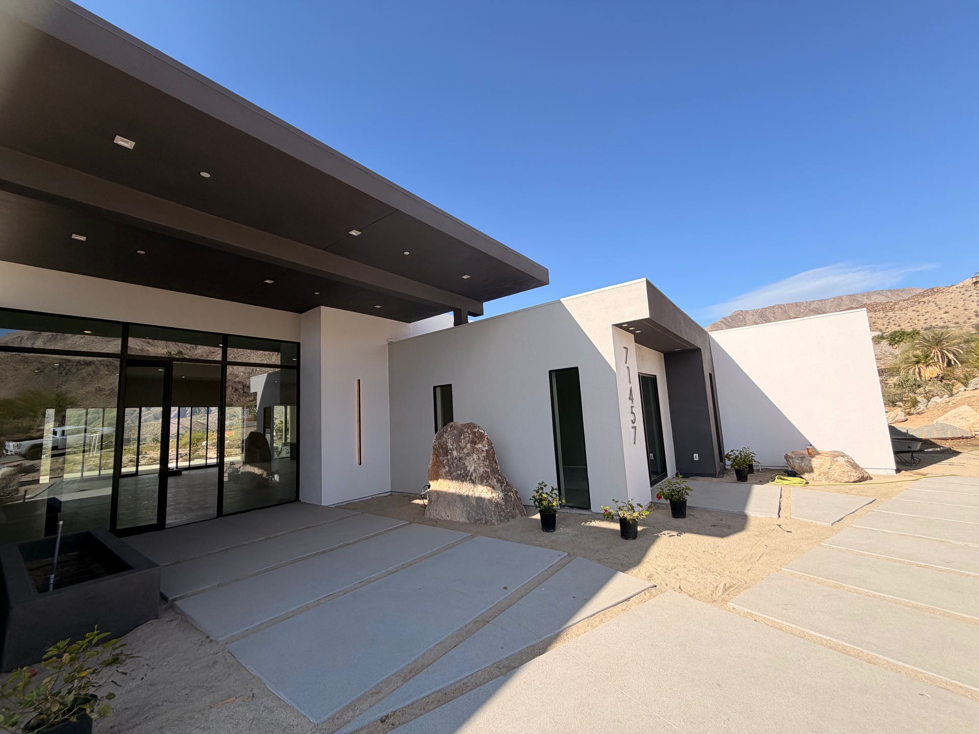 Modern house exterior with white walls, dark overhang, and desert landscaping under a clear blue sky
