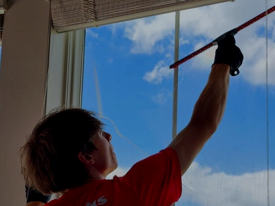 A man in a red shirt is cleaning a window with a squeegee in dublin ohio