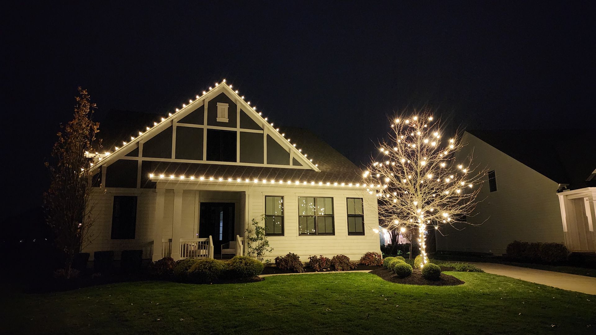 A white house with christmas lights on it is lit up at night.