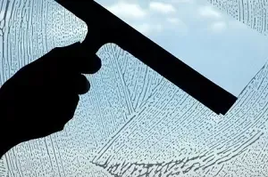 A man in a red shirt is cleaning a window with a squeegee.