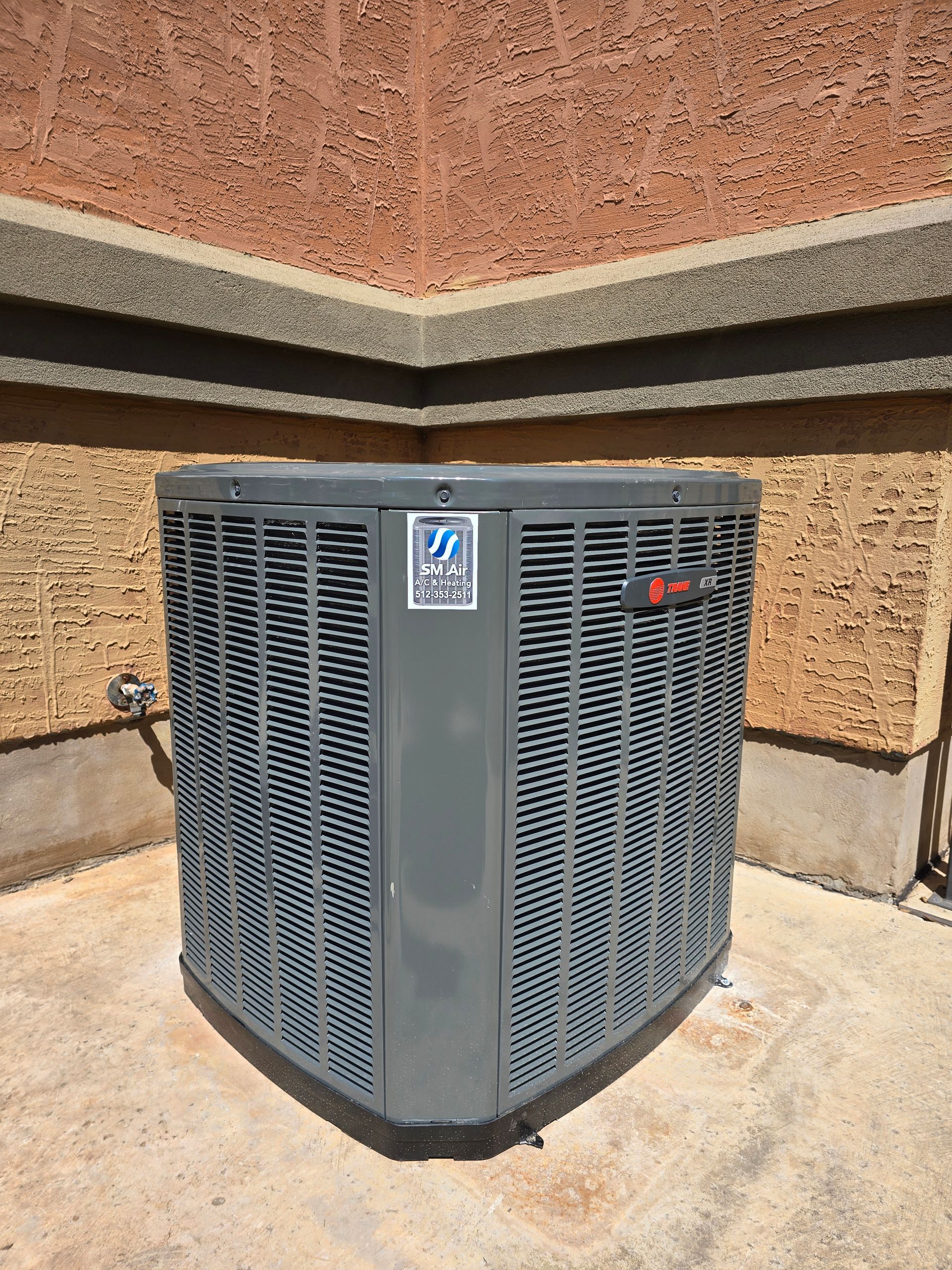 Outdoor HVAC unit against a building wall, gray metal with black vents and red indicator light.