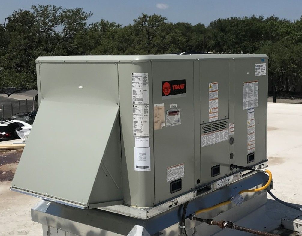 Large gray rooftop HVAC unit with open access panel on a flat roof.