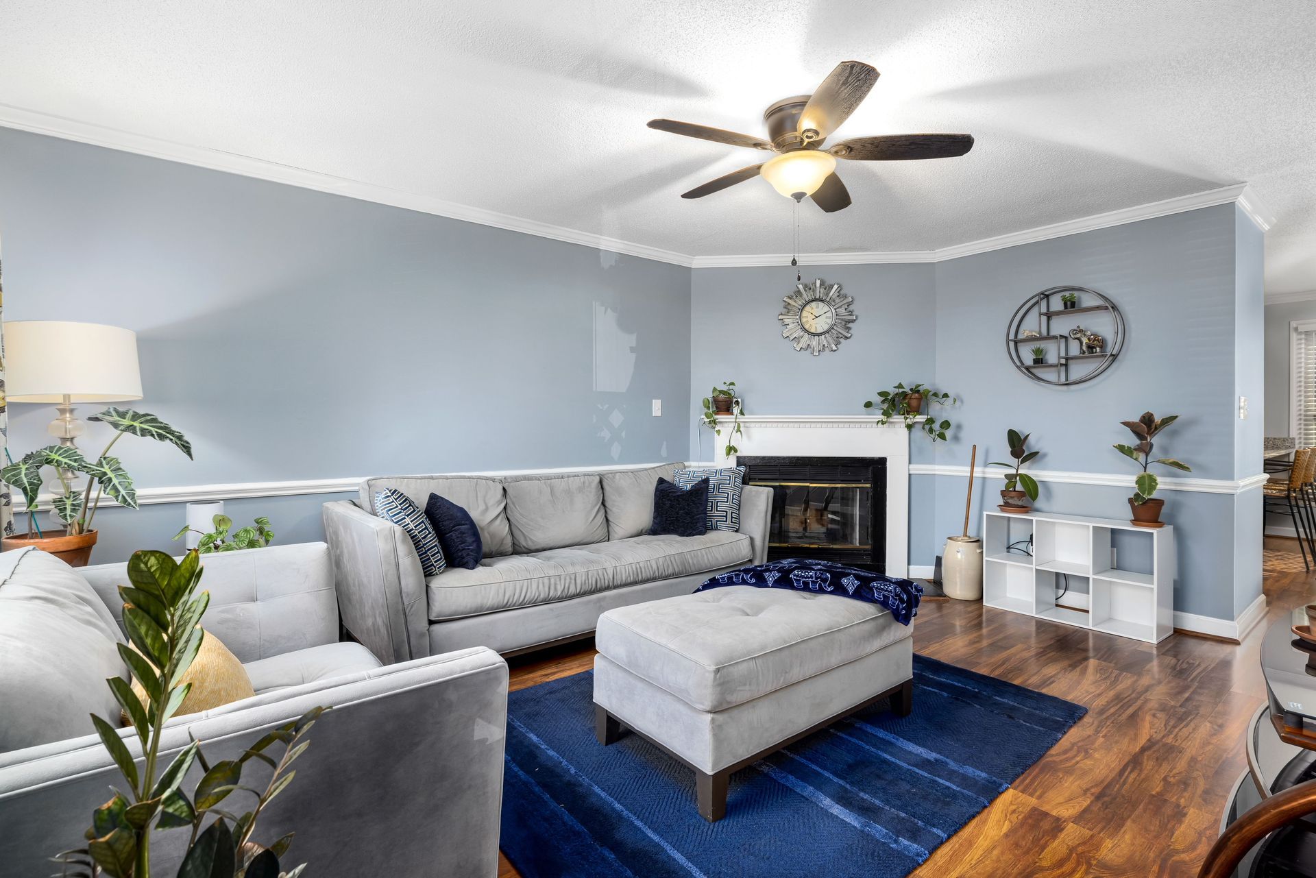 Bright living room with gray sectional, blue rug, fireplace, ceiling fan, and wood floors