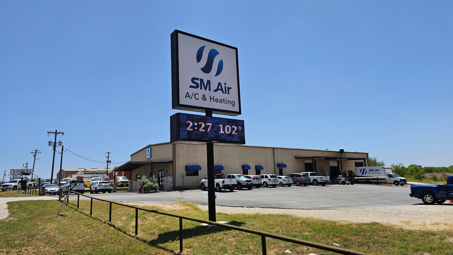 SM Air sign outside a low beige building on a sunny day with parked cars and gravel lot