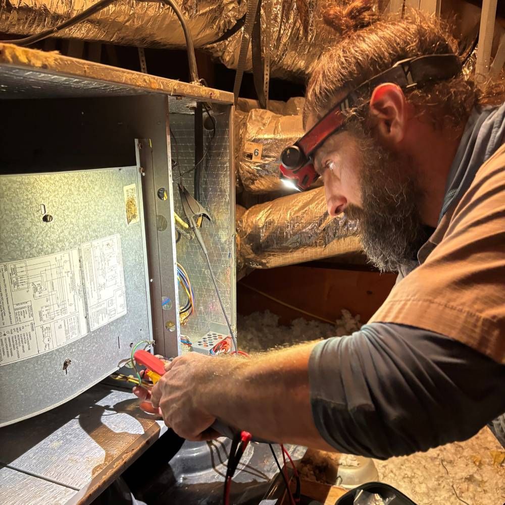 Technician inspecting HVAC unit with a multimeter in a dimly lit attic