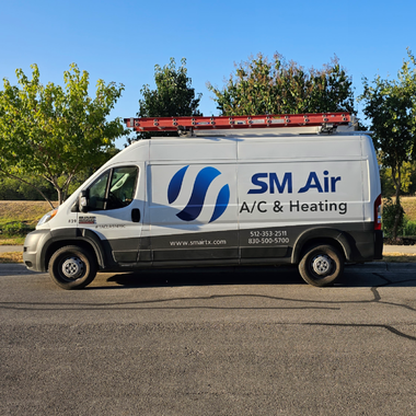 White SM Air HVAC service van parked on a street with a red ladder on the roof.