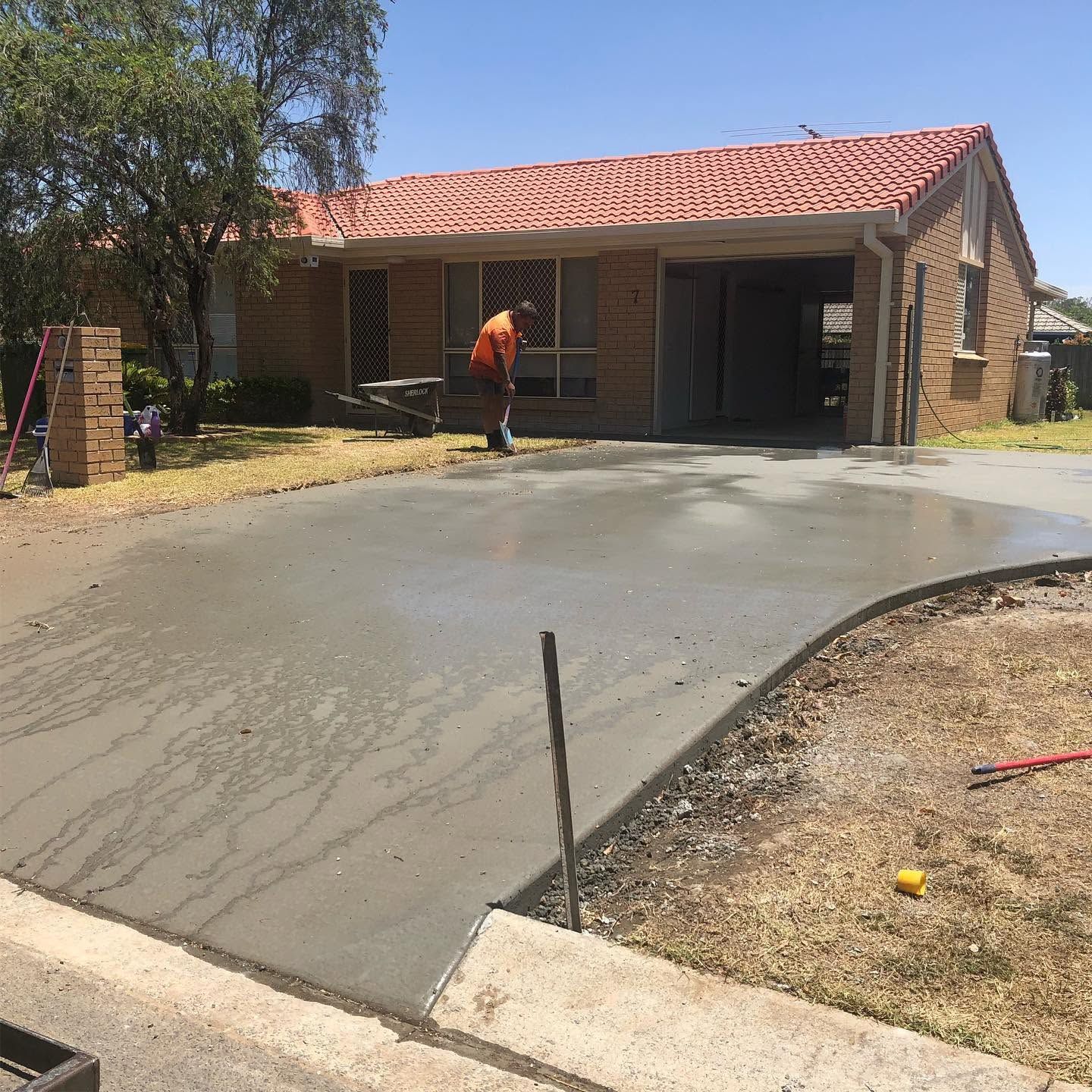 Fresh concrete driveway being smoothed in front of a brick house with a red-tiled roof
