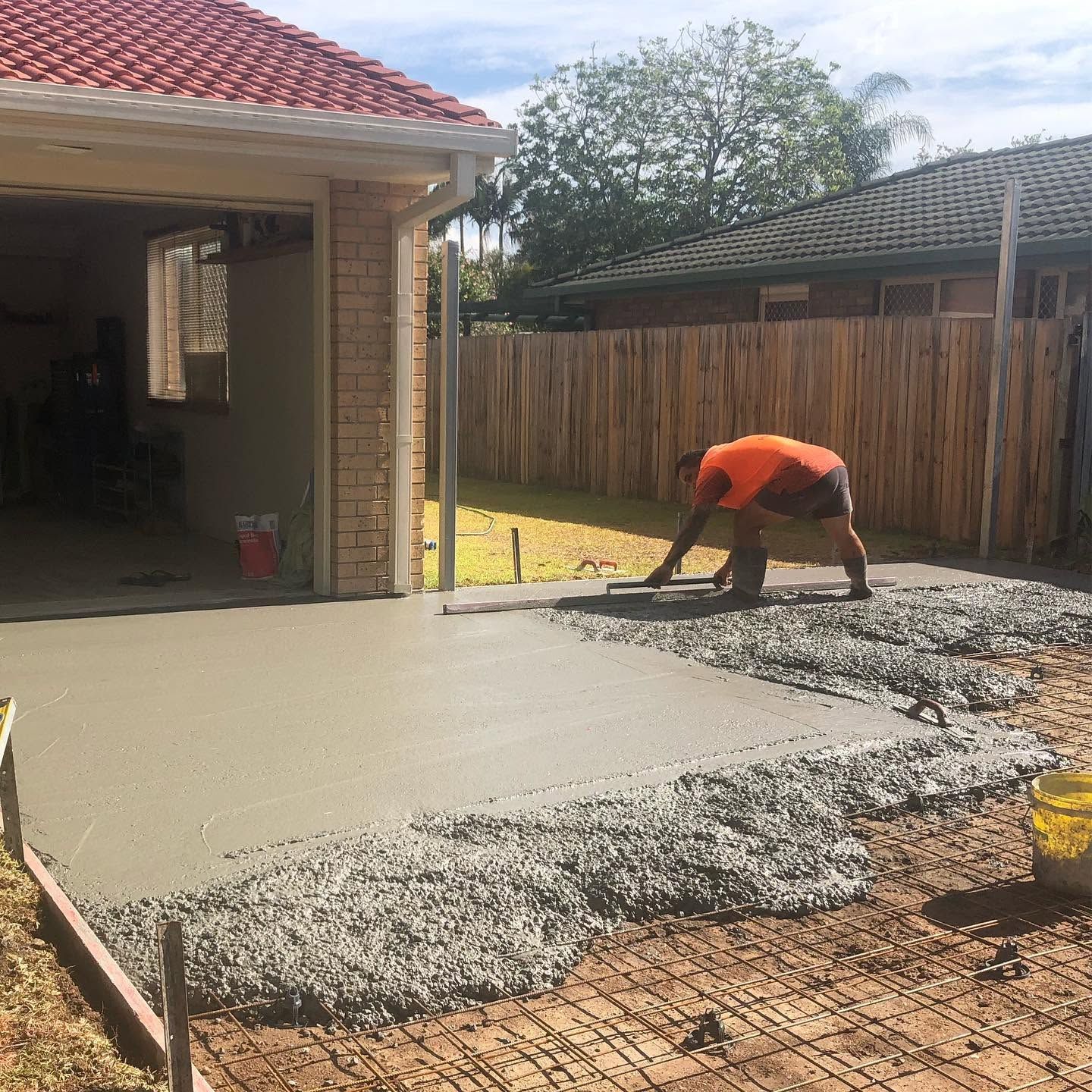Worker pouring concrete slab in a backyard beside a house and fence