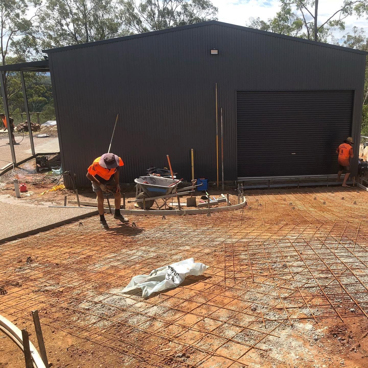 Workers preparing a construction site in front of a black metal building with a large garage door.