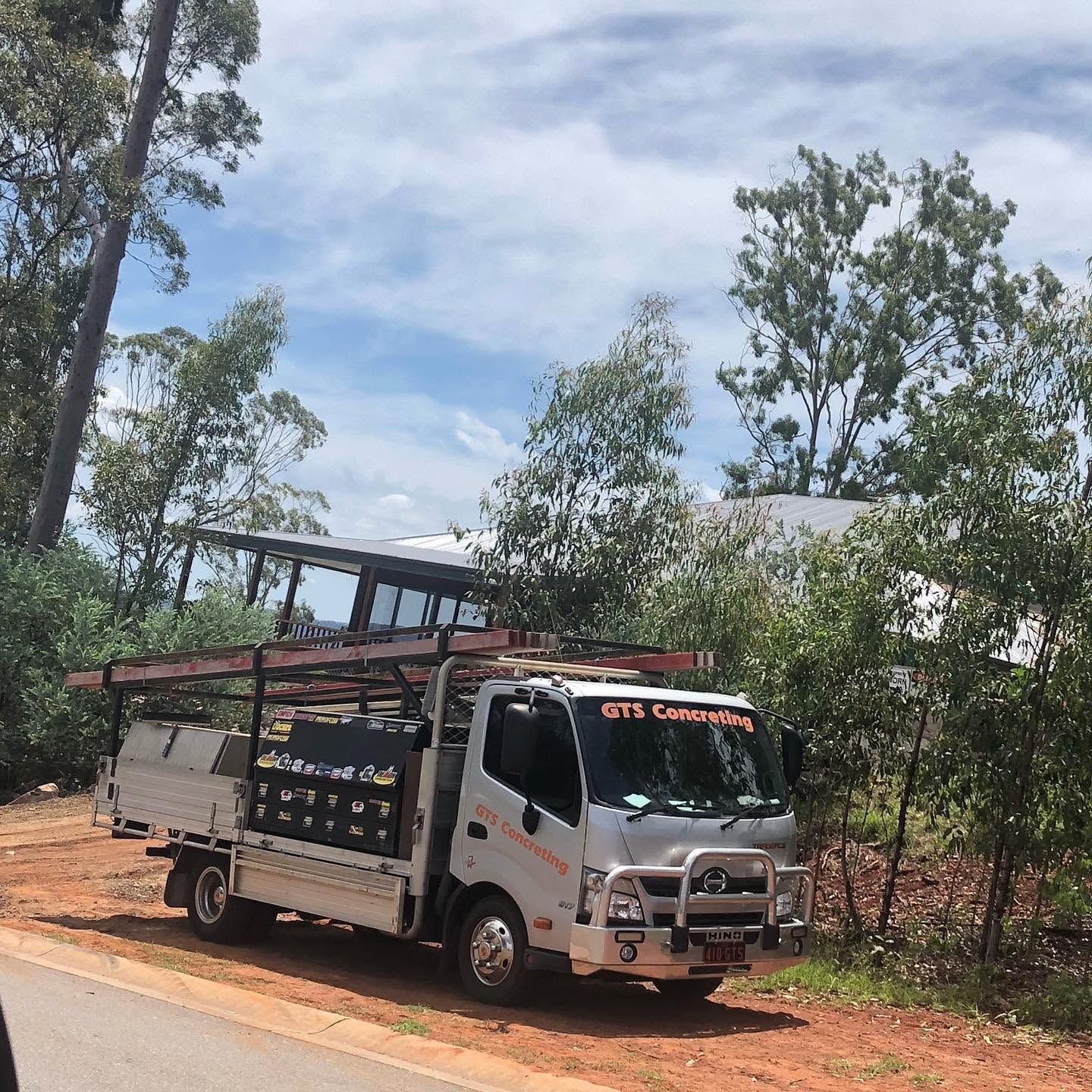 White flatbed truck on a dirt road beside trees under a partly cloudy sky